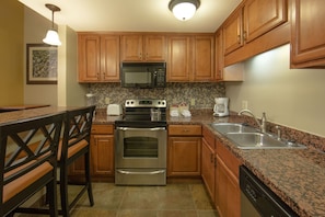 A kitchen with wooden cabinets, a stainless steel oven, a microwave, a granite countertop, and a dishwasher.