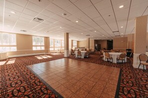 Un amplio salón de conferencias con alfombra estampada, varias mesas con sillas y grandes ventanales que dejan entrar luz natural.