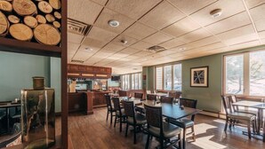 Un restaurante con suelo de madera, mesas, sillas, una zona de cocina y grandes ventanales.