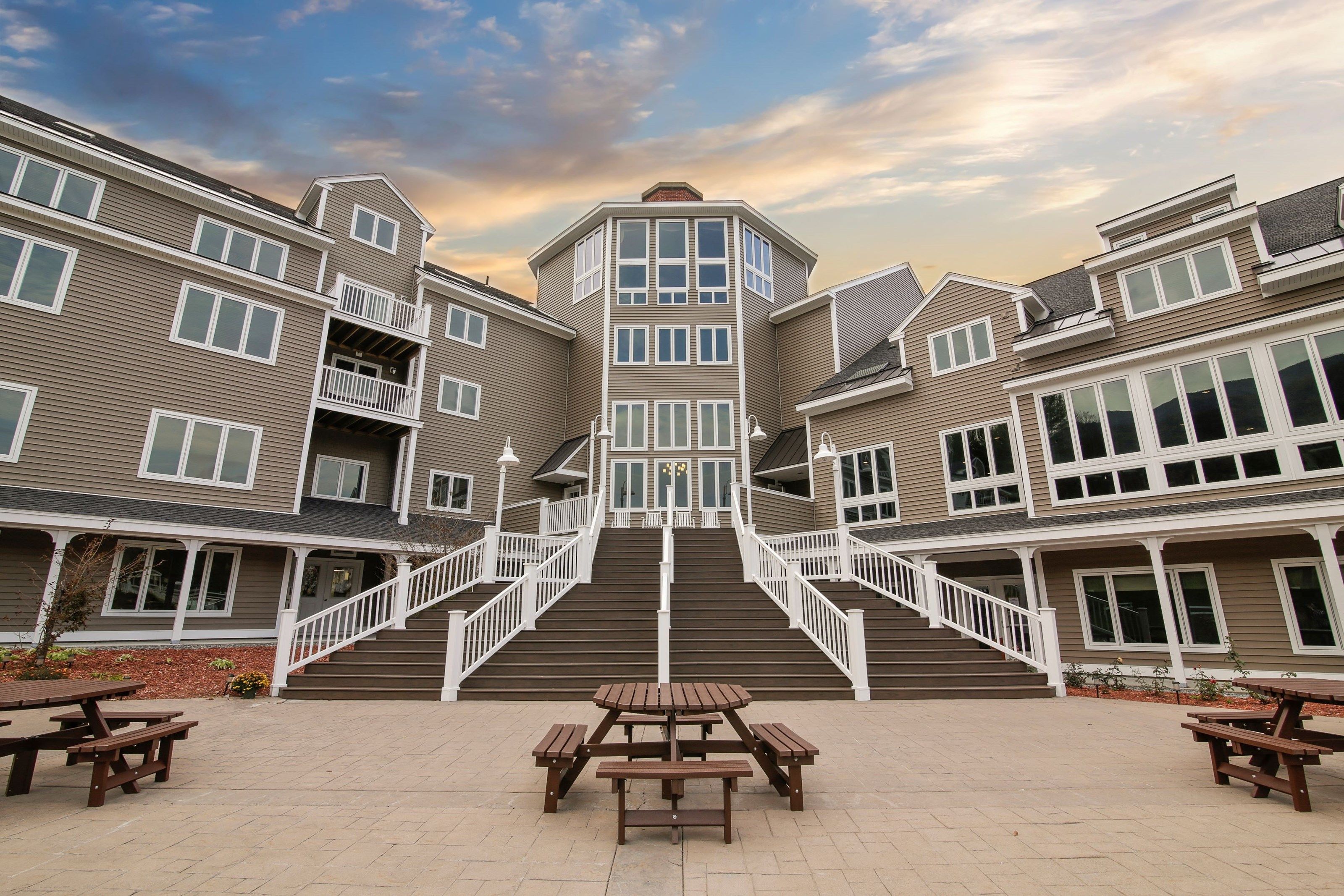A multi-story building with a central staircase, outdoor picnic tables, and a clear sky.