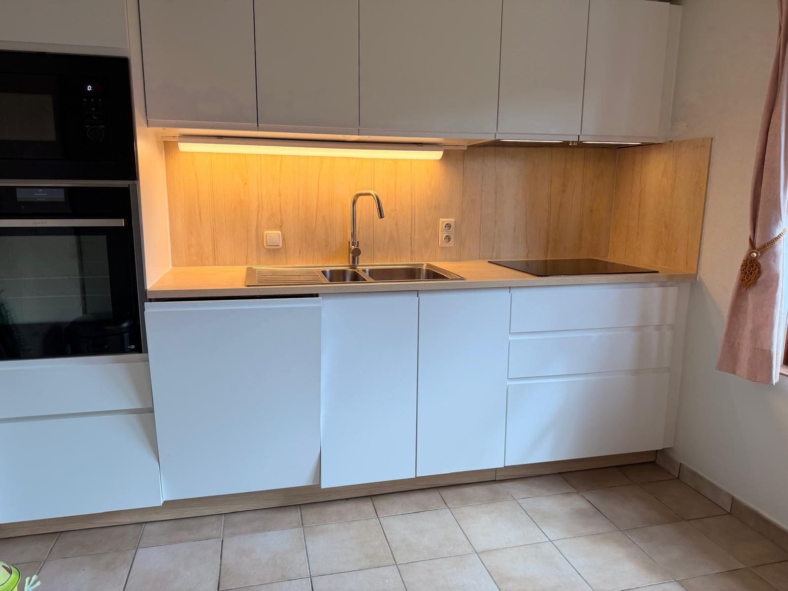 Eine moderne Küche mit weißen Schränken, einer Edelstahlspüle und einem eingebauten Backofen.