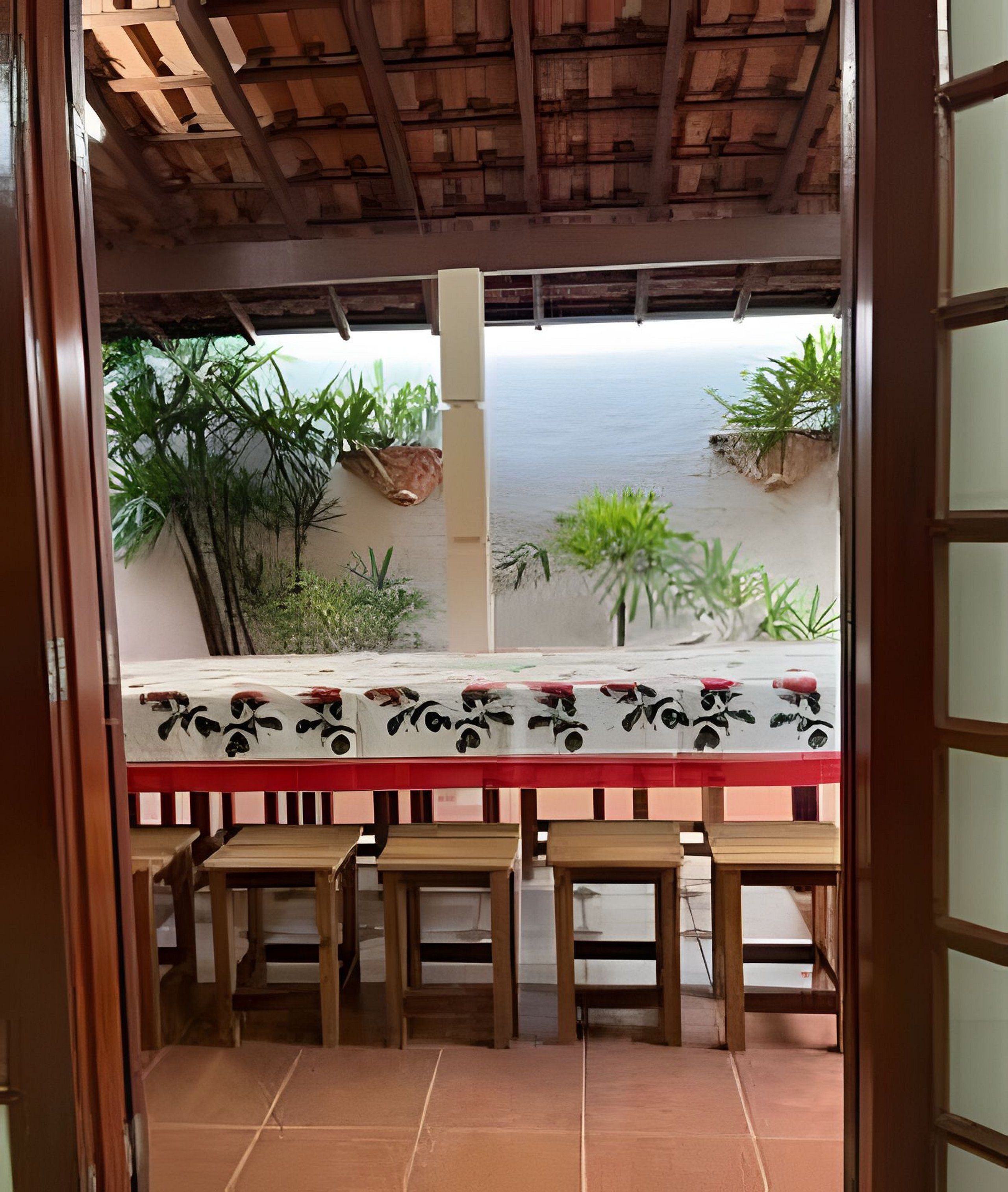 An outdoor dining area with a table and chairs, surrounded by plants and a view of the sea.