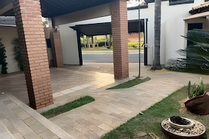 Un espacio al aire libre cubierto con pilares de ladrillo, un sendero pavimentado y un pequeño jardín con macetas.