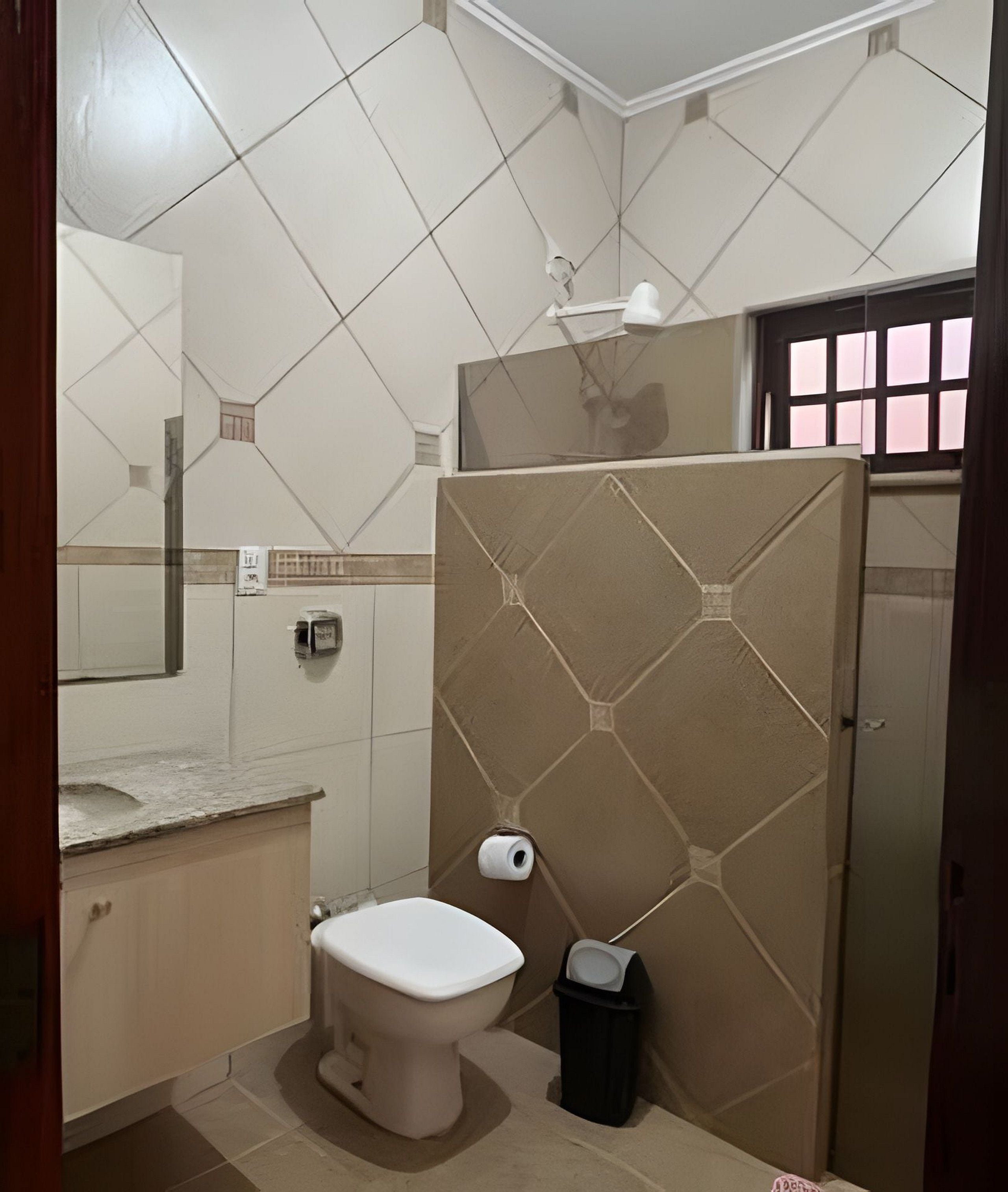 A bathroom with a toilet, a trash bin, a towel dispenser, and a mirror.
