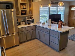 A modern kitchen with a stainless steel refrigerator, a microwave, and a toaster. There is a window with blinds and a sign that reads 'CALIFORNIA'. - Bright 2BR with Chef's Kitchen near Sony Studios (Culver City)