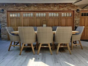 A dining area with a wooden table and wicker chairs, a stone wall, and a garage door. - Bright 2BR with Chef's Kitchen near Sony Studios (Culver City)