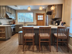 A modern kitchen with wooden cabinets, a central island with bar stools, and pendant lighting. - Bright 2BR with Chef's Kitchen near Sony Studios (Culver City)