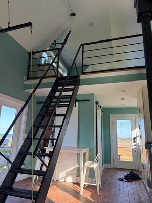 A multi-level interior with a staircase, a door leading outside, and a white chair. - Remote tiny home/loft overlooking the Roanoke Sound & the Outer Banks (Manns Harbor)