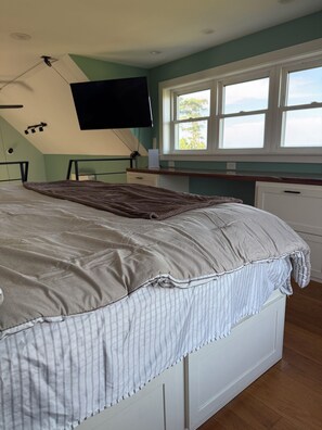 A bedroom with a bed, a window, and a flat-screen TV mounted on the wall. - Remote tiny home/loft overlooking the Roanoke Sound & the Outer Banks (Manns Harbor)