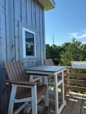 A wooden deck with a table and two chairs, a window, and a view of trees. - Remote tiny home/loft overlooking the Roanoke Sound & the Outer Banks (Manns Harbor)