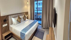 A hotel room with a bed, a desk, a chair, a TV, and a balcony with curtains. - Deluxe Shyam Bazar Guest House (Kolkata)