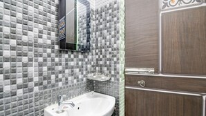 A bathroom with a white sink, a mirror, and a tiled wall. - Deluxe Shyam Bazar Guest House (Kolkata)