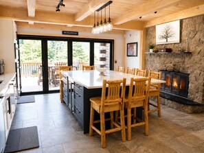 Una cocina amplia con una isla grande, sillas de madera, una chimenea de piedra y vistas al exterior.