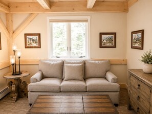 Una habitación acogedora con un sofá color beige, un aparador de madera, una mesita redonda con una lámpara y cuadros en las paredes.