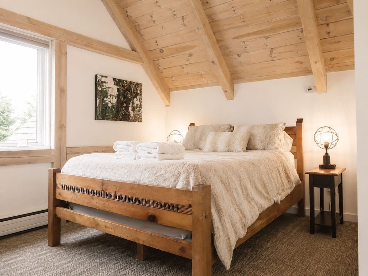 A bedroom with a wooden bed, a bedside table with a lamp, and a window with a view.