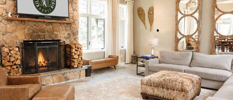 Amplio salón con chimenea de piedra, mobiliario de cuero y un ventanal que proporciona luz natural.