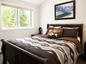 A bedroom with a large bed, a nightstand, a window with a view of trees, and a framed picture on the wall. - Slopeside Estate Guesthouse: Hot tub, AC, Grill (Killington)
