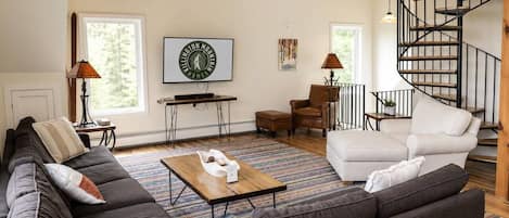 Una sala de estar moderna con un sofá seccional gris oscuro, un sillón blanco, una mesa de centro de madera y una escalera espiral.