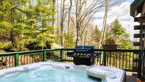 Een hottub op een houten terras, met een barbecue en planten in potten op de achtergrond.