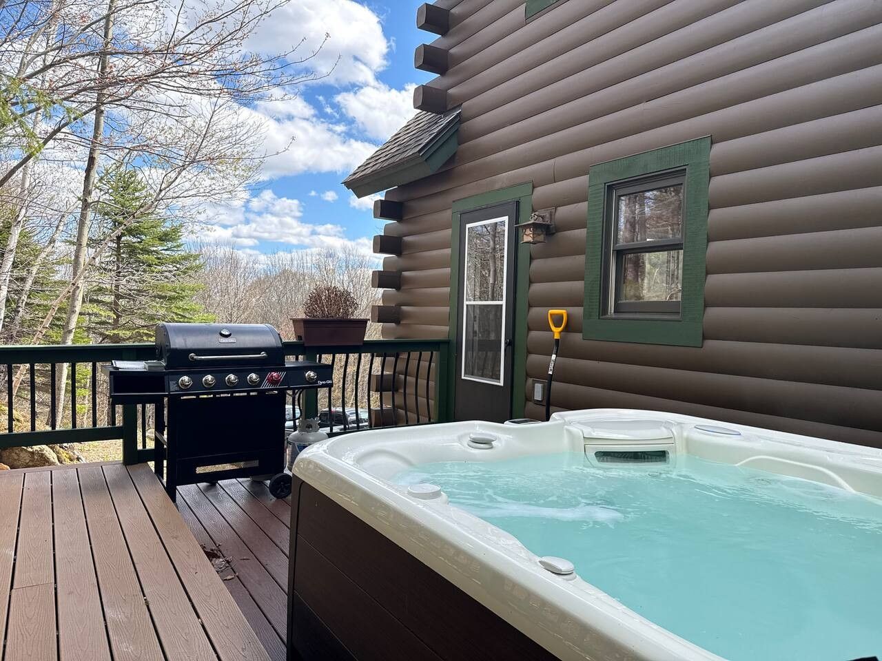 A wooden deck with a hot tub, barbecue grill, and a small table.