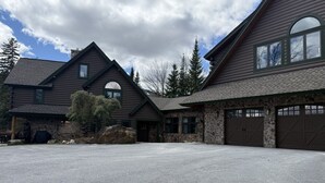 Een chalet van hout met twee verdiepingen, een stenen fundering, een garage en een brede oprit met grind.