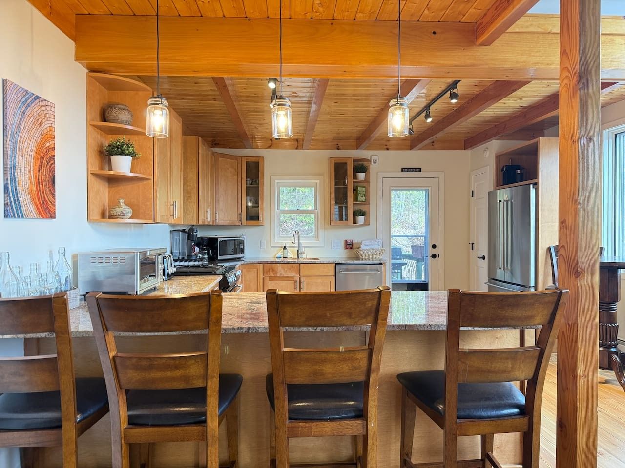 Interior em madeira com cozinha, mesa de jantar e cadeiras, e iluminação pendente.