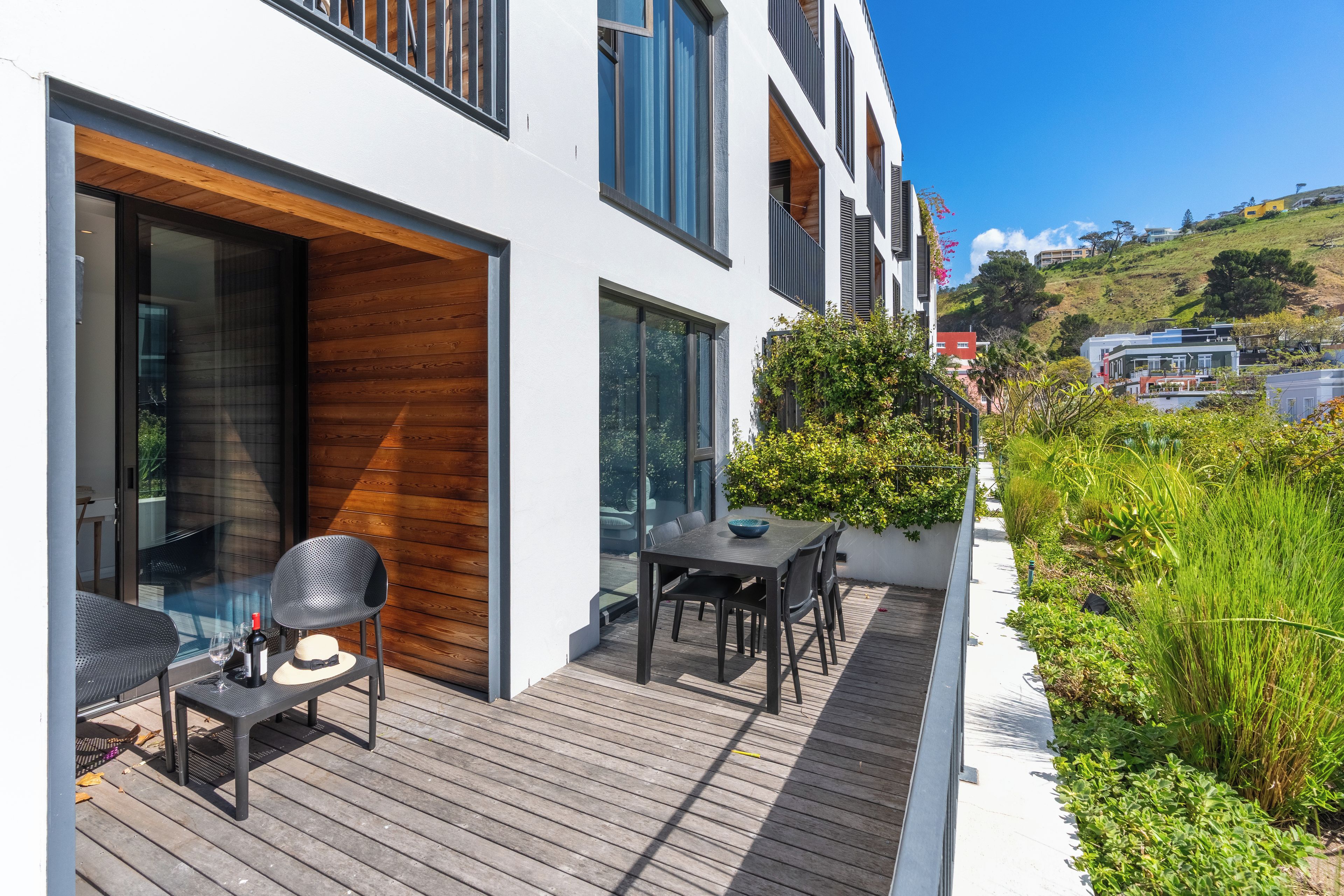 A modern house with a wooden deck, outdoor seating, and a view of the surrounding landscape.