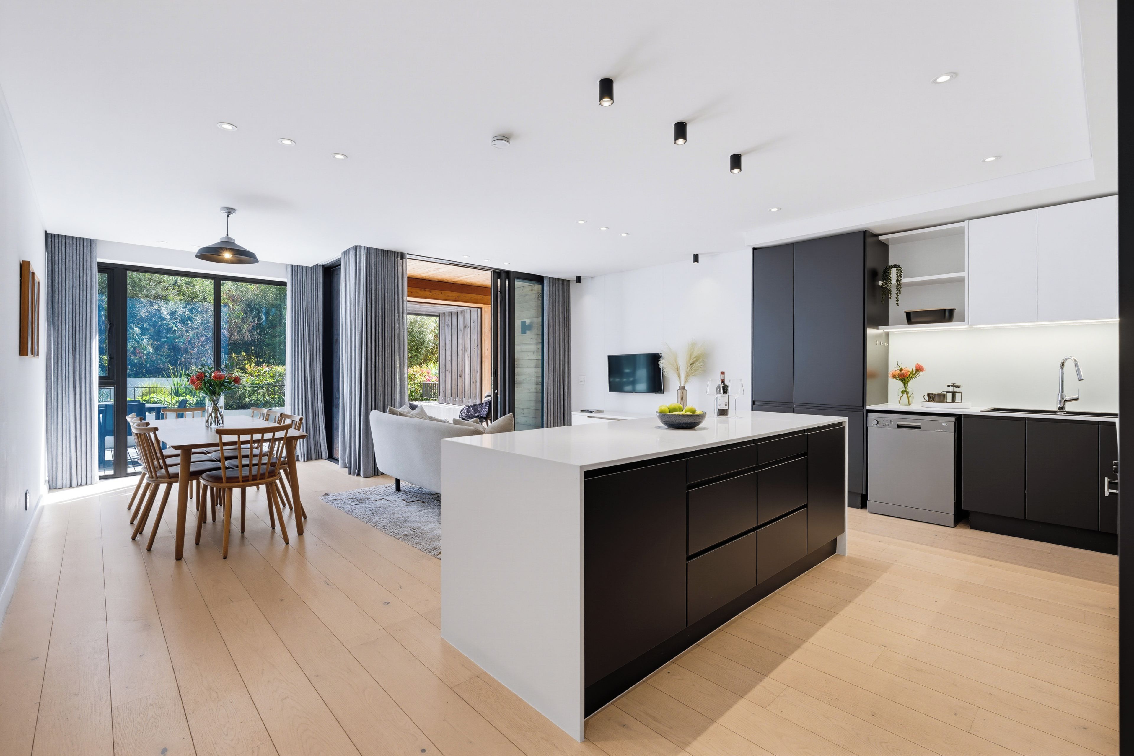 A modern kitchen with a central island, dark cabinetry, and a dining area with a table and chairs.