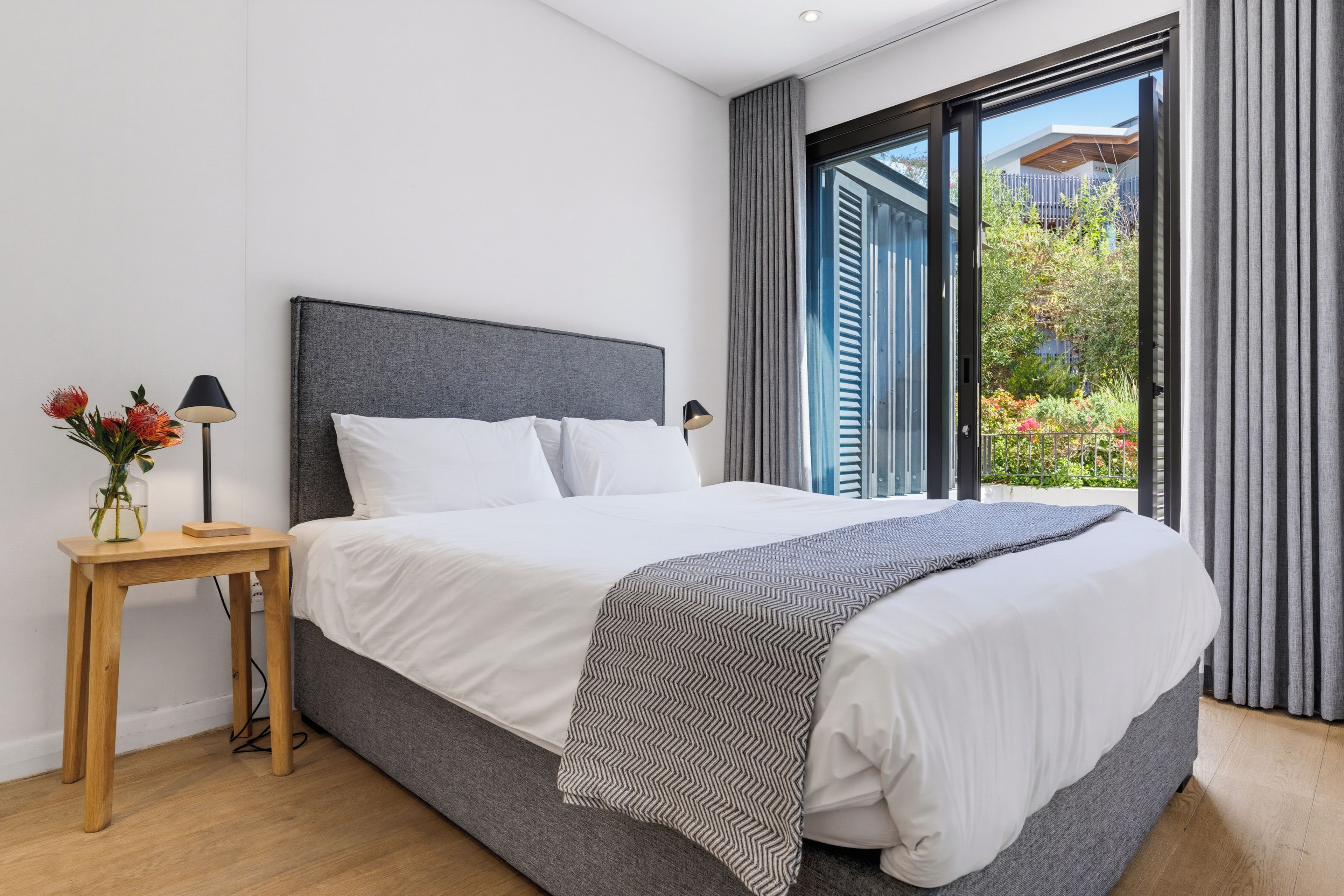 Ein modernes Schlafzimmer mit einem großen Bett, einem Nachttisch und Blick auf Grünfläche.