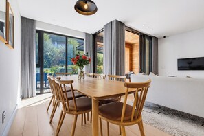 Un comedor moderno con una mesa y sillas de madera, ventanas amplias y vistas al exterior con vegetación.