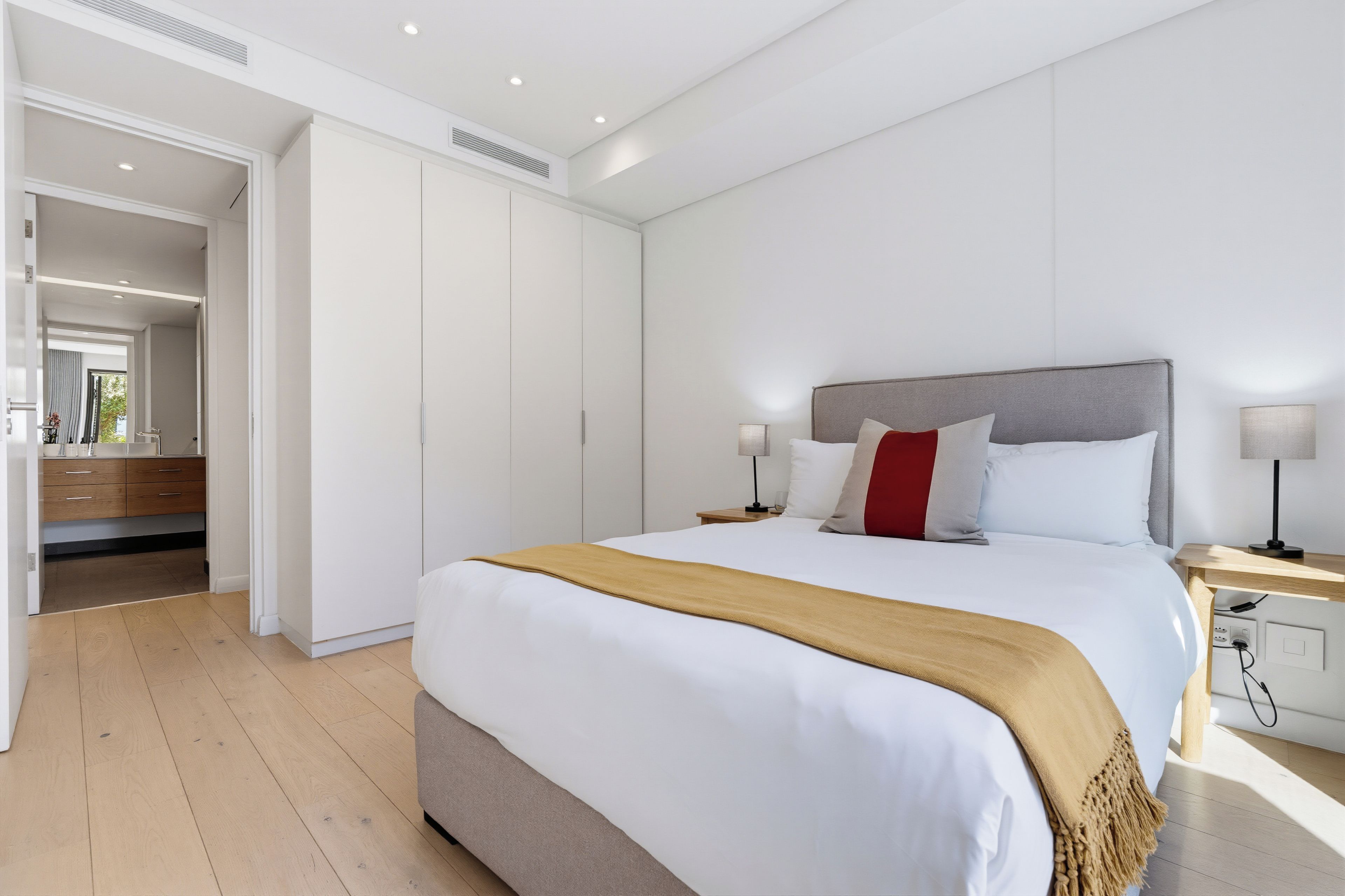 A modern bedroom with a large bed, bedside tables, a wardrobe, and a bathroom visible through an open door.