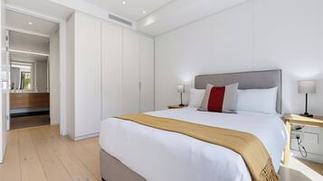 A modern bedroom with a large bed, bedside tables, a wardrobe, and a bathroom visible through an open door.
