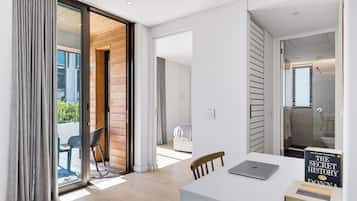 A modern interior with a sliding glass door leading to a balcony, a white desk with a laptop, and a book titled 'The Secret History' by Donna Tartt.