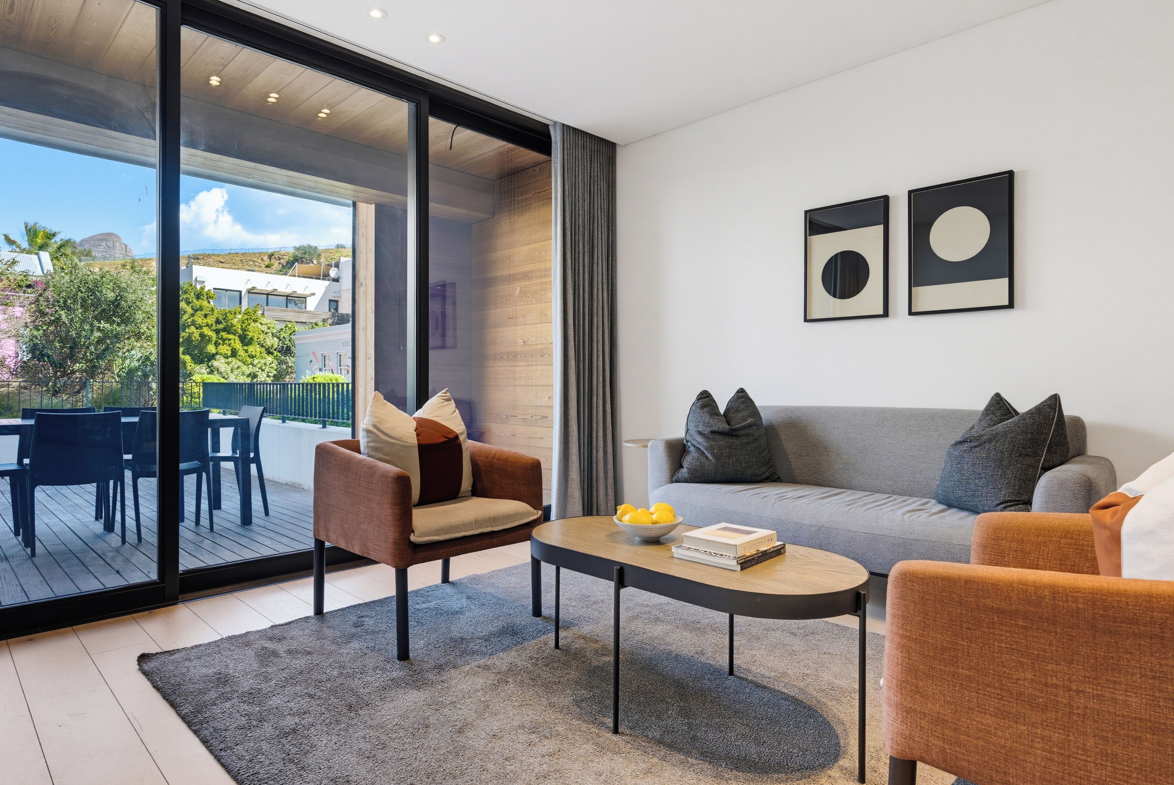 A modern living room with a sofa, armchairs, a coffee table, and a large window offering a view of the outdoors.