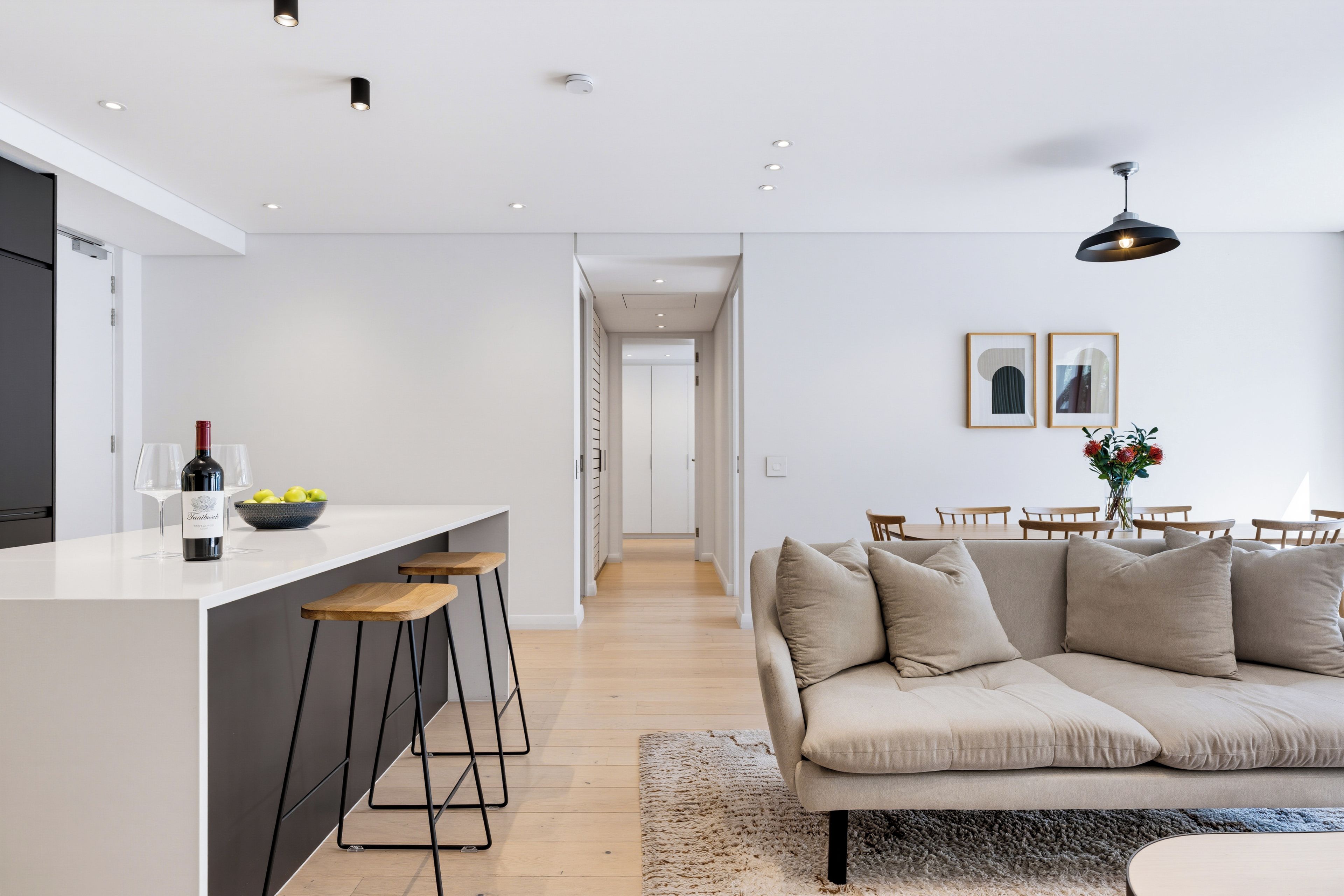 Cocina moderna con una isla central, taburetes de bar y una zona de comedor con sofá y sillas.