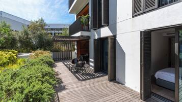 Une terrasse extérieure moderne, dotée d’un pont en bois, d’un espace salon avec des chaises et une table, et d’une porte vitrée donnant accès à une chambre.