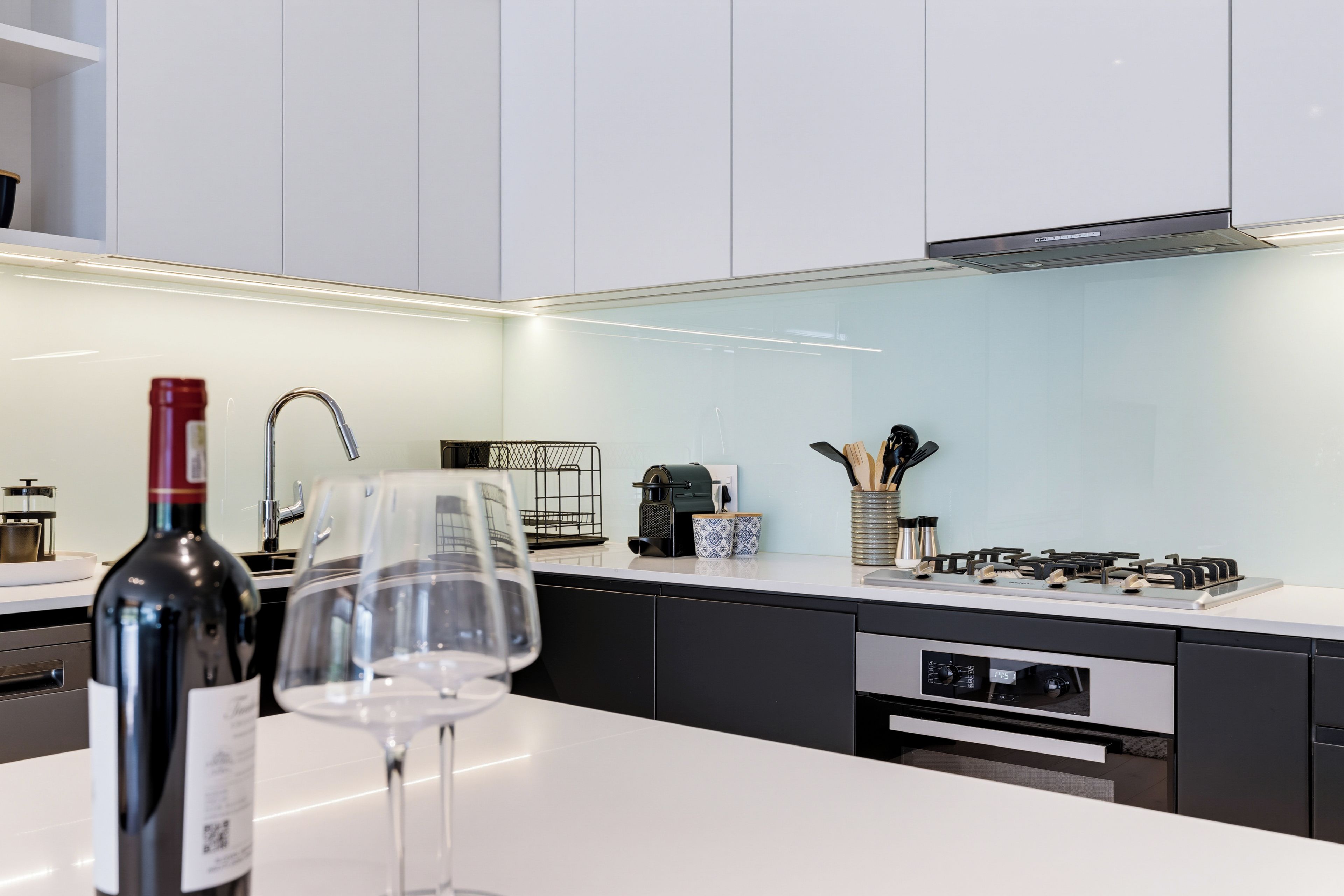 Een moderne keuken met witte kasten, een wijnfles en een wijnglas op het aanrecht.