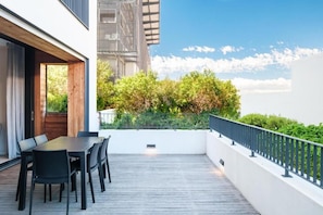 Eine Terrasse im Freien mit Esstisch und Stühlen, umgeben von einer weißen Mauer und einem schwarzen Geländer.