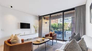 Una sala de estar moderna con un televisor de pantalla plana, un sofá, una mesa de centro y una zona de comedor con sillas.