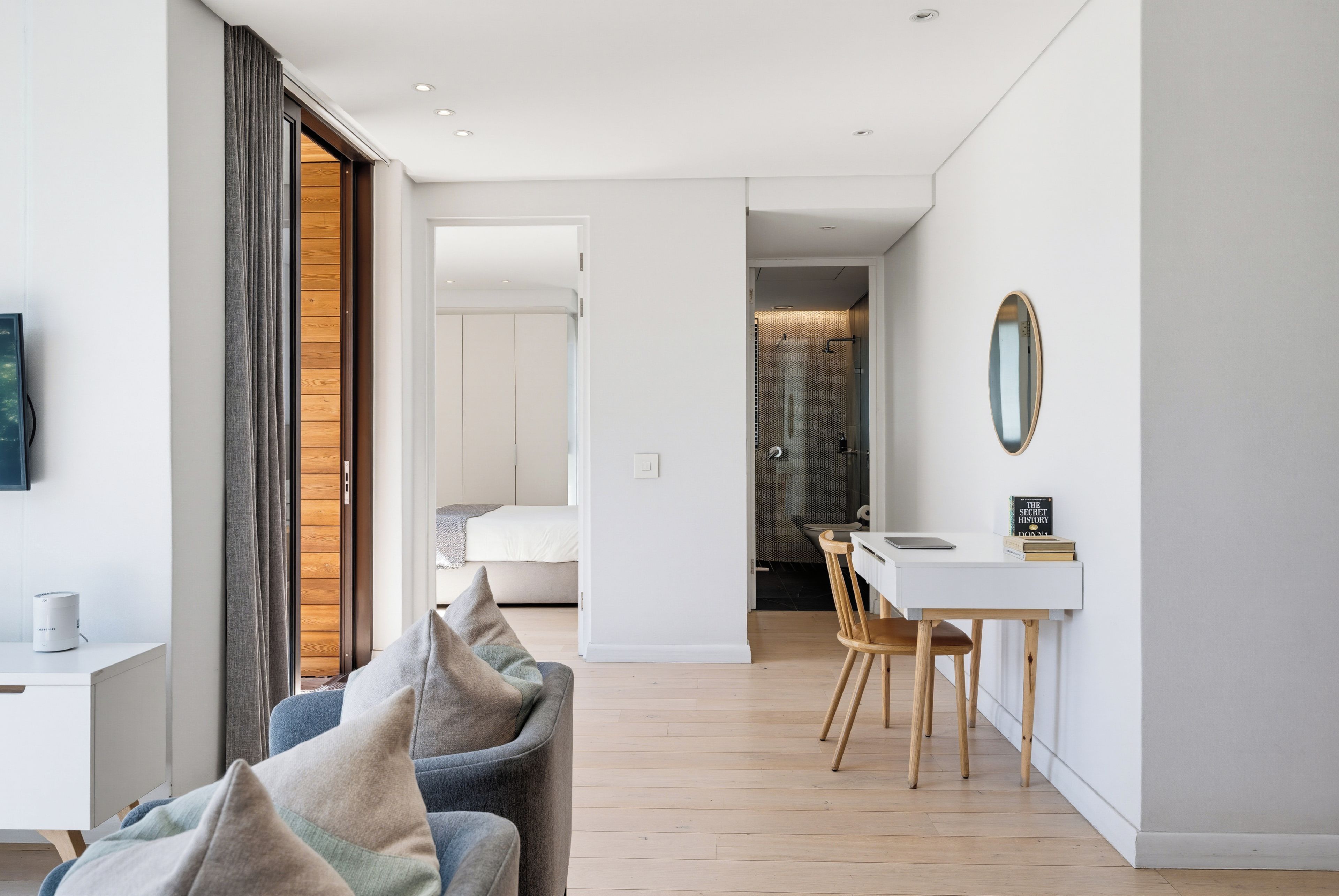A modern living room with a sofa, a dining area with a table and chairs, and a bedroom visible through an open door.