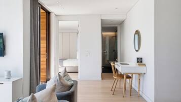Een moderne woonkamer met een bank, een eethoek met tafel en stoelen, en een slaapkamer zichtbaar door een open deur.