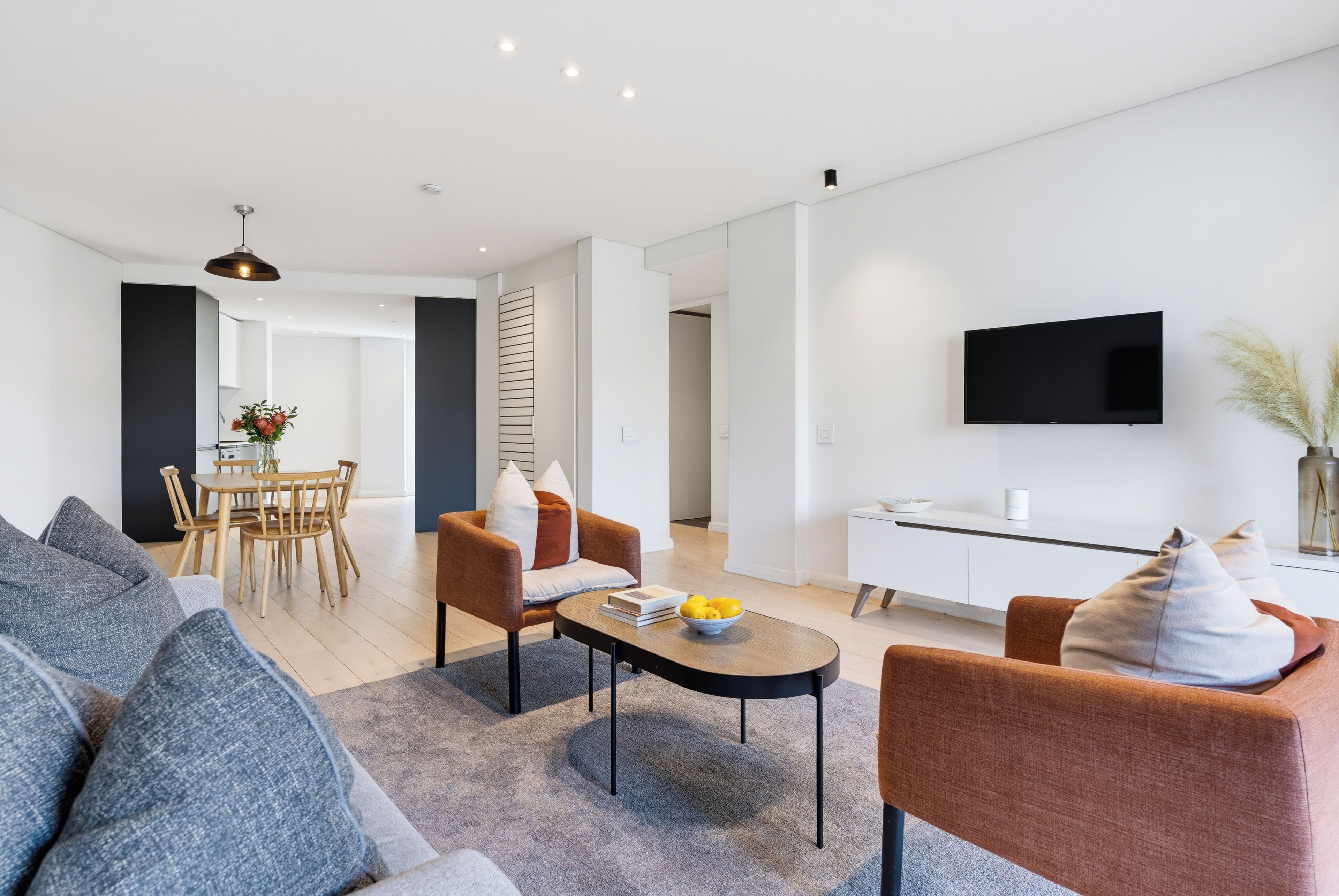 A modern living room with a sofa, armchairs, a coffee table, and a dining area with chairs and a table.