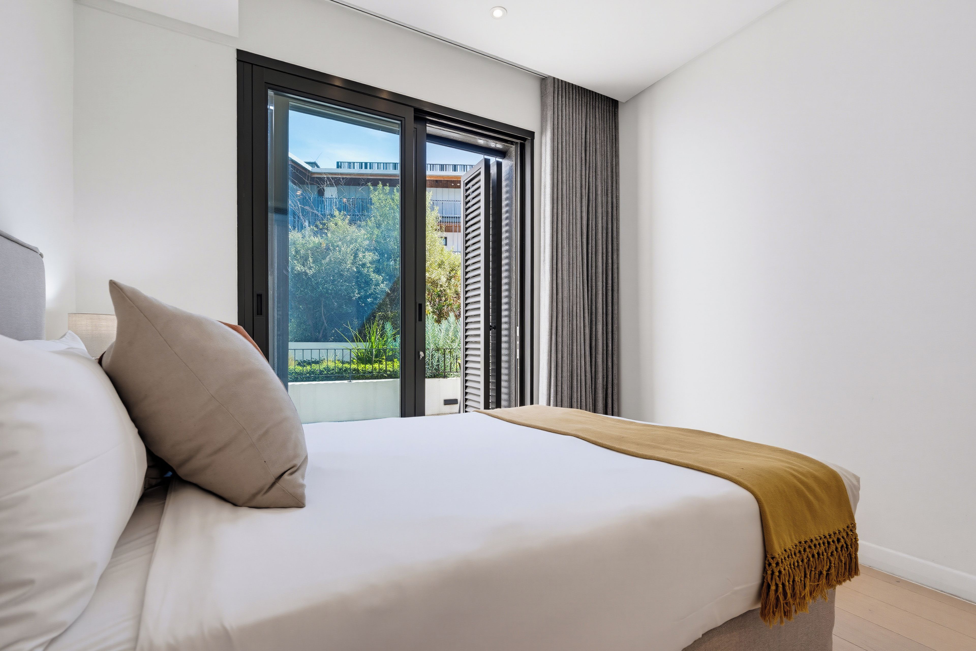 A modern bedroom with a large bed, a view of a balcony, and a window with curtains.