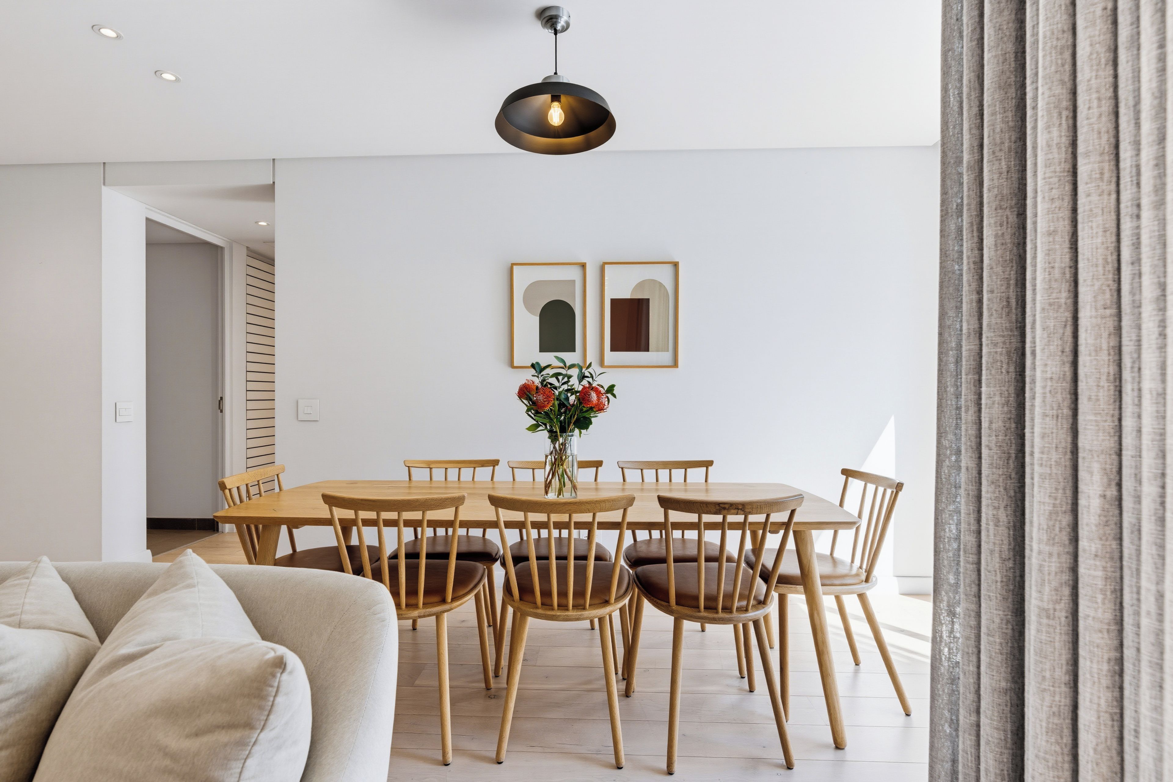 Un coin repas avec une table et des chaises en bois, un vase rempli de fleurs et deux tableaux encadrés accrochés au mur.