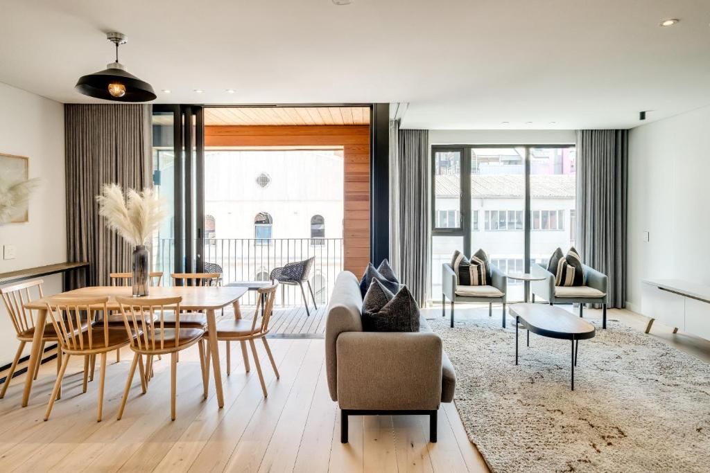 A modern living room with a sofa, chairs, a dining table, and a large window.