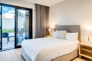 Ein Hotelzimmer mit einem großen Bett, einem Nachttisch, einer Lampe und einer Glastür, die zu einem Außenbereich mit einem Stuhl führt.