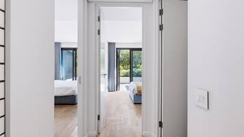 Un couloir mène à deux chambres dotées de grandes fenêtres, d’un plancher en bois et offrant une vue sur la verdure environnante.