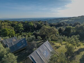 A rural landscape with a clear view of the horizon, a few trees, and a small building with a sloped roof. - Glamping Pagliaini (Riparbella)