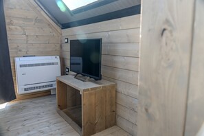 A room with a wooden wall, a television on a wooden stand, and an air conditioning unit.