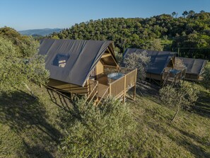 A series of wooden cabins with sloped roofs, surrounded by natural vegetation and hills in the background.